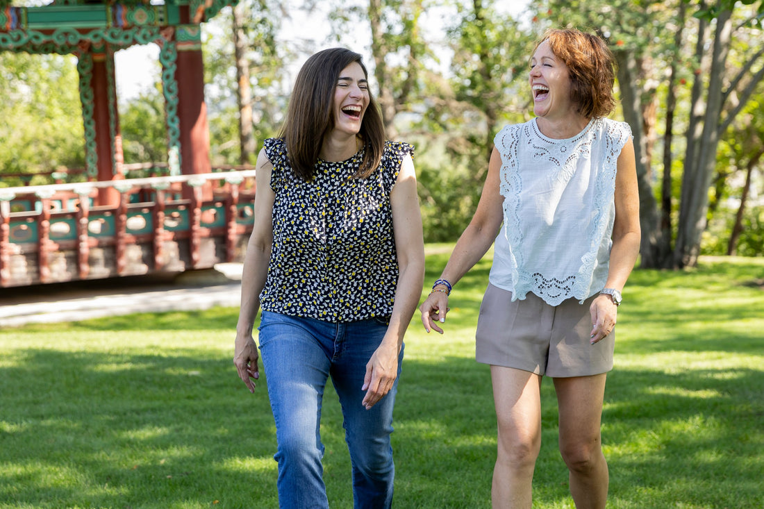Two mamas laughing together on a sunny walk in the park